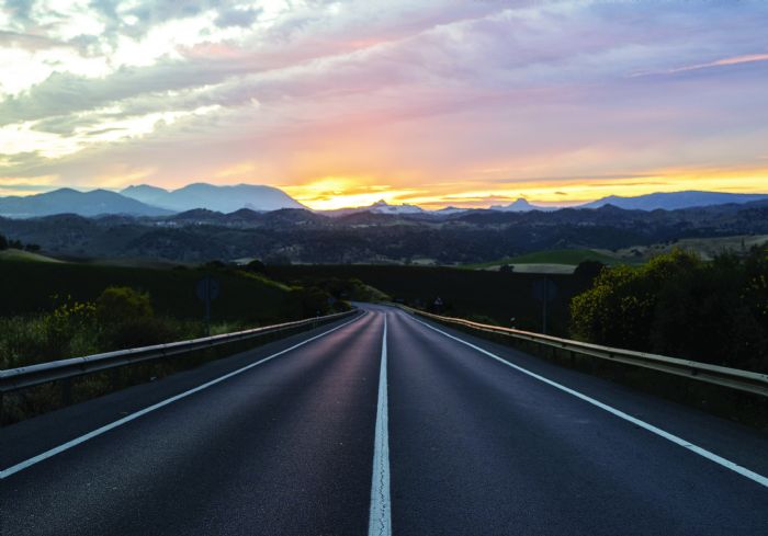 empty-highway-surrounded-by-hills-cloudy-sunset-sky